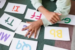 Criança manipulando cartões com letras coloridas em atividade lúdica de alfabetização e reconhecimento do alfabeto.