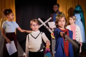 Crianças participando de atividade de teatro escolar, usando fantasias e encenando uma peça que estimula criatividade, expressão e trabalho em equipe.