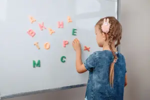 Criança organiza letras coloridas em quadro magnético durante atividade de alfabetização.