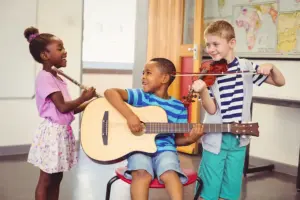 Crianças participando de atividade de musicalização na educação infantil com violão, flauta e violino em sala de aula.
