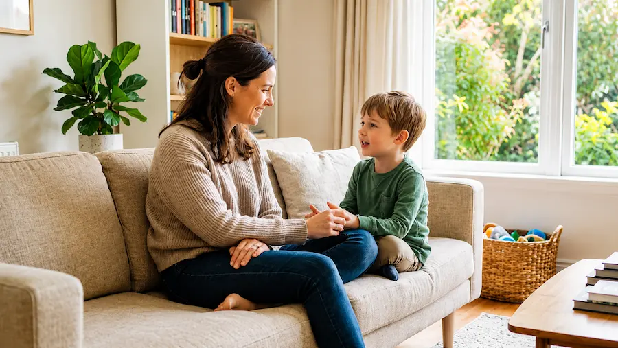 Mãe conversa com o filho sentado no sofá em um ambiente familiar, representando diálogo e vínculo na parentalidade positiva.